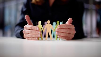 Hands safeguarding paper models representing workplace employees