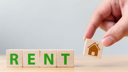 Children's letter blocks spelling out the word rent with hand holding a house block