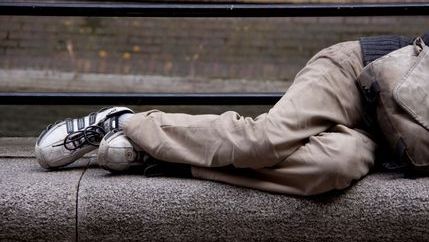 Legs of a homeless man lying on a stone bench
