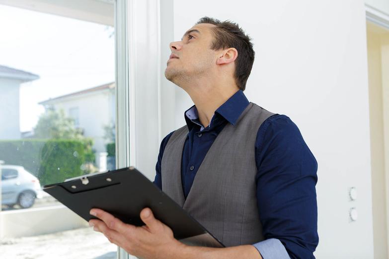 Man holding a clipboard and inspecting the windows of a property