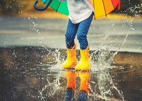 Girl in yellow wellies jumping in puddle holding umbrella