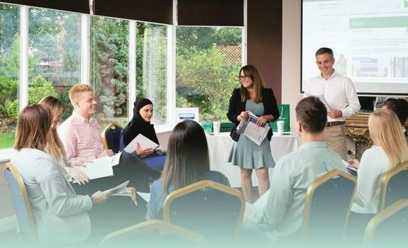 Group of people sat in a circle looking towards trainer with a presentation in the background