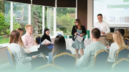 Group of people sat in a circle looking towards trainer with a presentation in the background