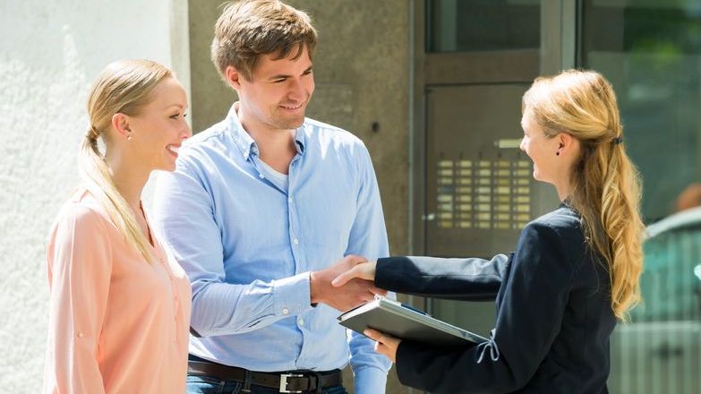 Agent shaking hands with couple outside a property