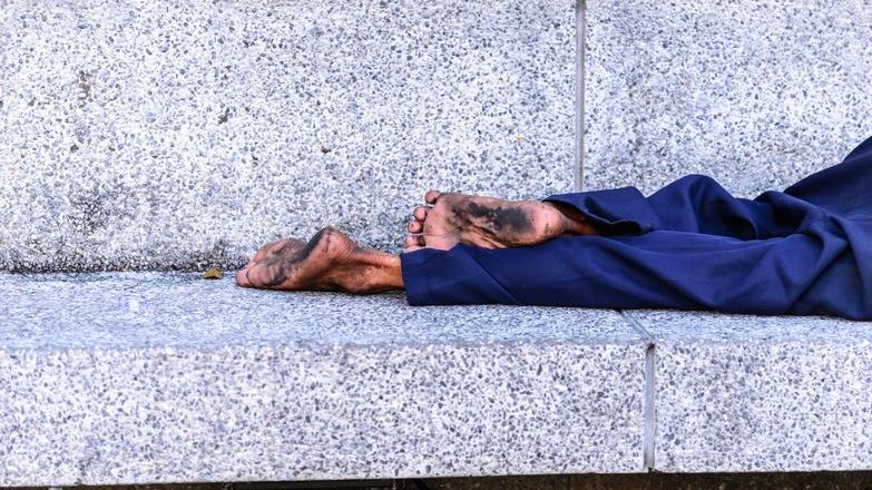 barefoot homless person lying on stone bench