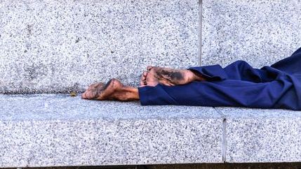 barefoot homless person lying on stone bench