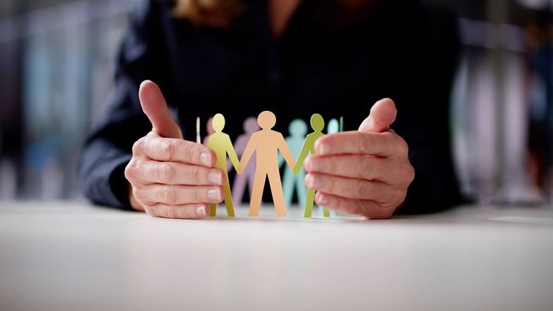 Hands safeguarding paper models representing workplace employees