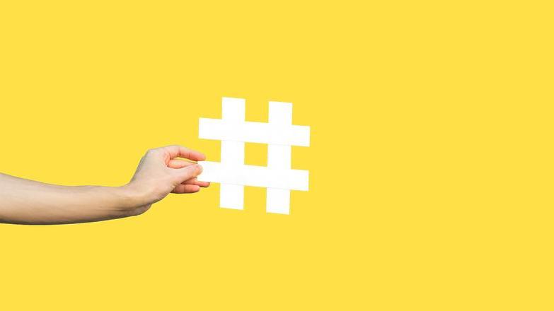 Hand holding up a hashtag symbol against yellow background