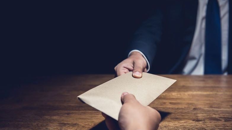 A man giving bribe money in a brown envelope to another businessman in the dark