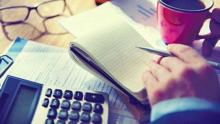 Person making notes with calculator and coffee