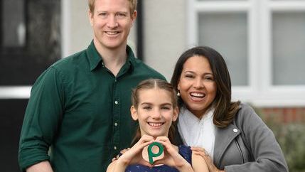 Young family holding P in front of house