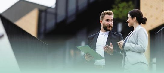 Professional man and woman in discussion with smart, modern looking property in the background 